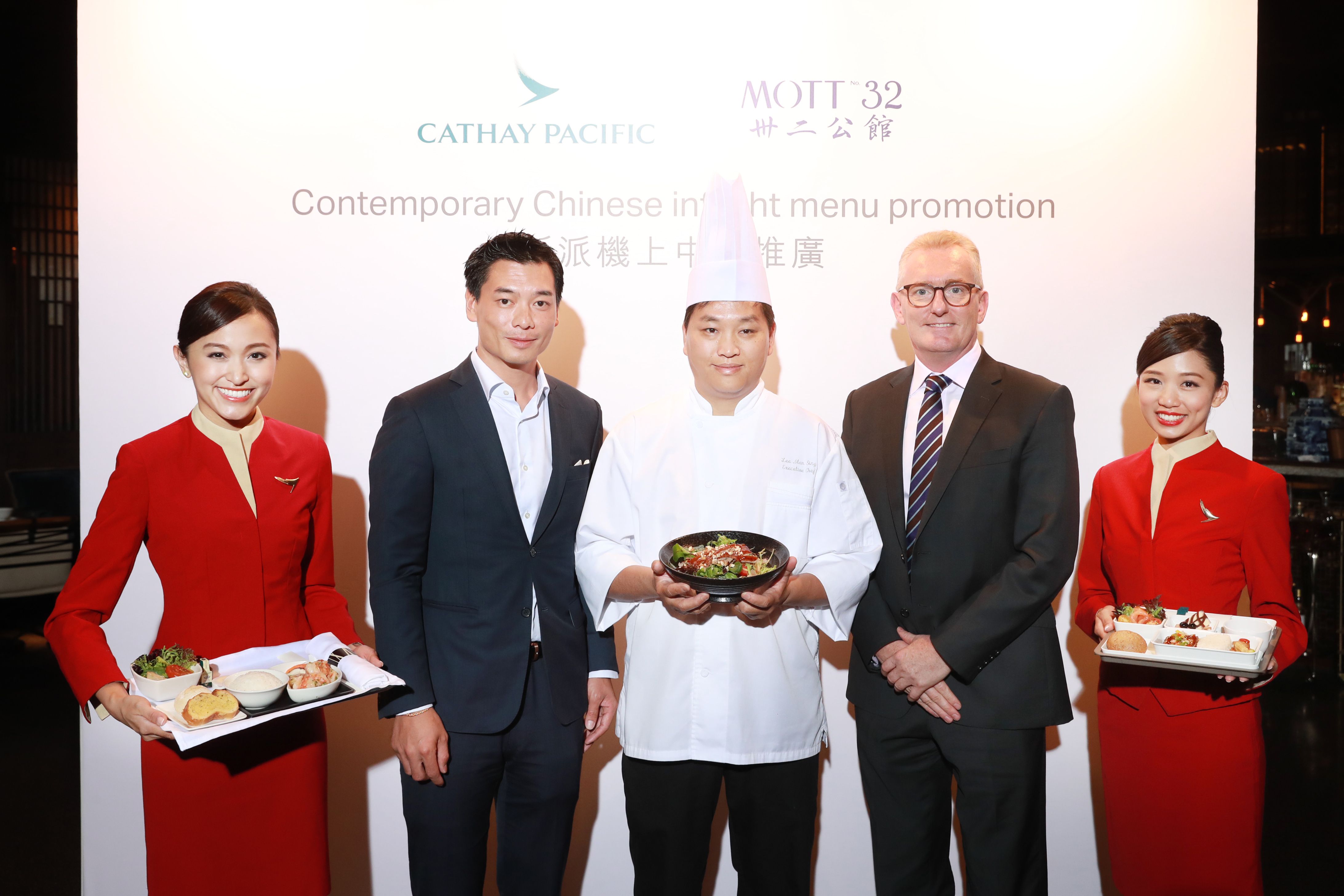 Cathay Pacific Head of Catering Aaron Claxton (second from right), Founder and Managing Director of Maximal Concepts Xuan Mu (second from left) and Chinese Group Executive Chef Lee Man-sing (middle) pose with the new Mott 32 dishes showcased by Cathay Pacific cabin crew.
