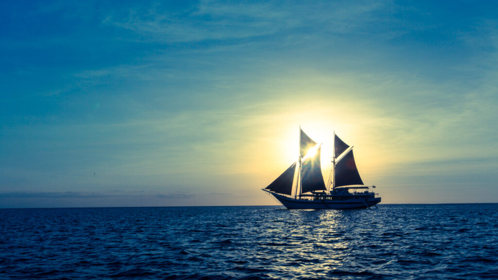 Sailing ship Ombak Putih silhouetted against the sun while cruising indonesia.