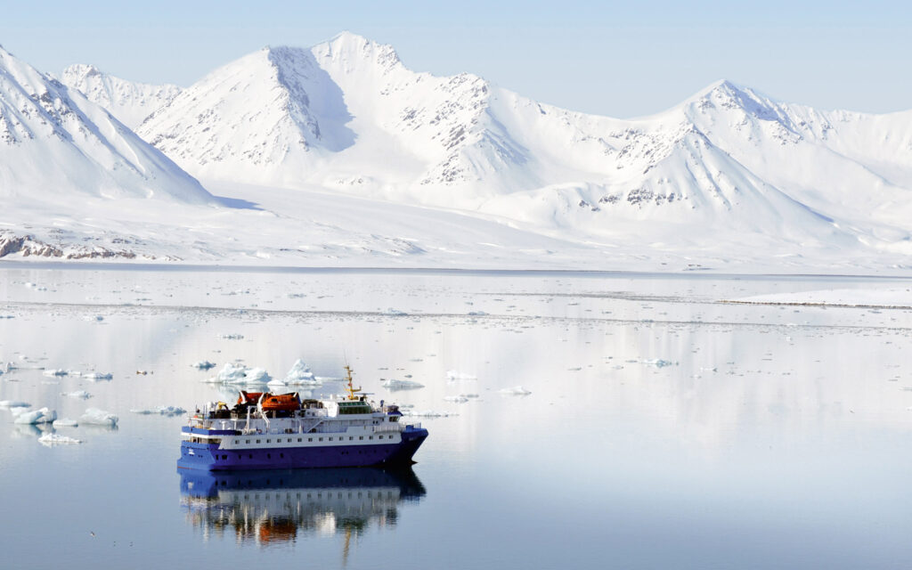 Small cruise ship exploring the arctic on a calm day in front of white snowy mounatins.