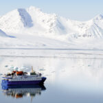 Small cruise ship exploring the arctic on a calm day in front of white snowy mounatins.