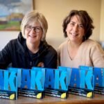 Two women behind a counter covered with trophies